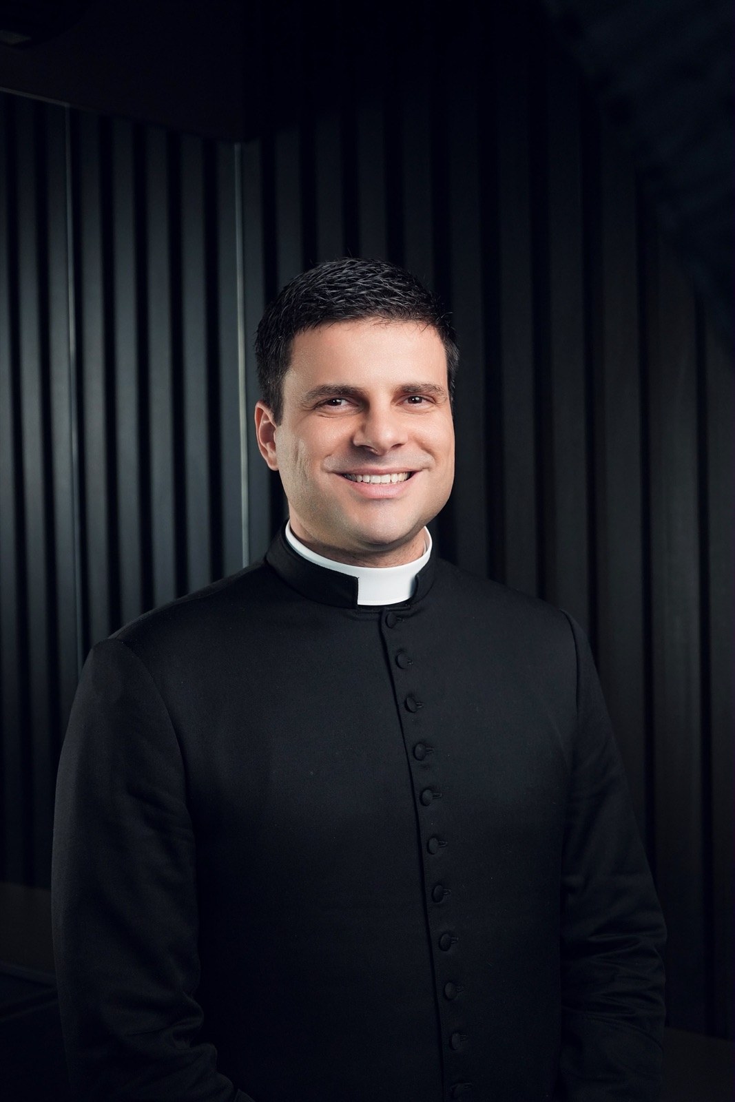 Padre Pedro Faustino sorrindo, vestido com batina preta